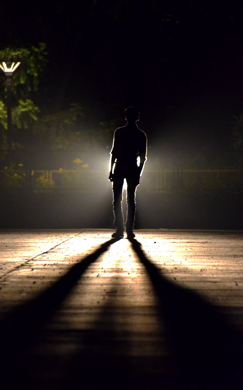 unrecognizable man on shining wooden walkway illuminated by street light
